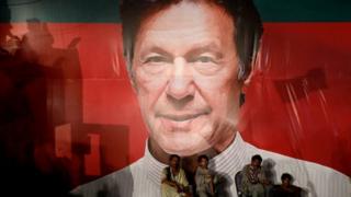 Para buruh duduk di depan poster Imran Khan ketua partai Pakistan Tehreek-e-Insaf (PTI).