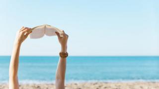 Una mujer lee un libro en la playa.