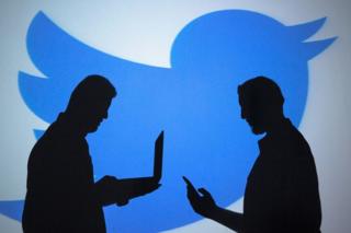 El perfil de dos hombres con lapton y celular frente a un logo de Twitter