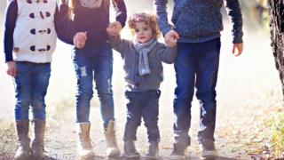 stock image of a little boy holding hands with his two older siblings, and a fourth child alongside