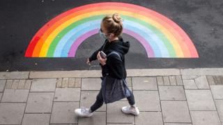 Woman in a mask walks past a rainbow painted on the floor