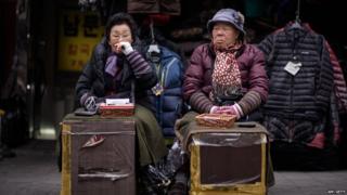 Two currency exchange vendors sit before their stalls as they wait for customers at a market in Seoul