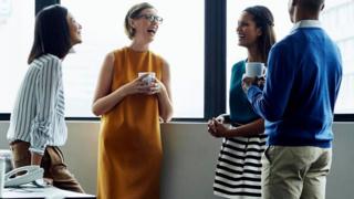 Cuatro trabajadores de pie, tomando café y conversando