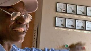 John Mwafute next to a row of dials in his power station