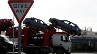 Transporter lorry carrying new cars drives behind give way sign