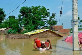 An Indian resident carries gas canisters as he wades through a flooded area following heavy monsoon rains in Muzaffarpur in the Indian state of Bihar.