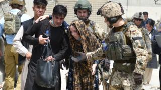 Soldiers help a woman, who fell due to high temperature at the Kabul International Airport as thousands of Afghans rush to flee the Afghan capital of Kabul