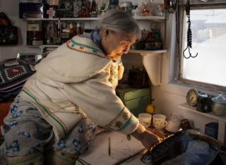 Town elder Qapik Attagutsiak washing up in her traditional hut