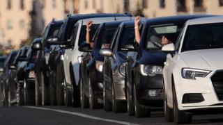 Menschen in Autos hupen und zeigen ihre Hände mit weißen Bändern - Symbolen der Proteste - am Handgelenk