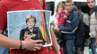 Мигрант держит фотографию канцлера Германии Ангелы Меркель после прибытия беженцев на главный железнодорожный вокзал в Мюнхене, южная Германия, 15 сентября 2015 года