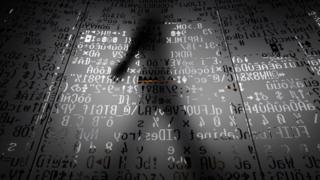 Sombra de un hombre tras códigos informáticos