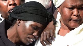 Akon Guode, (L), closes her eyes and rests her arm on another woman, after the children's funeral in 2015