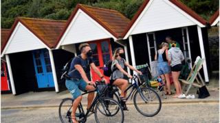 Cyclists wearing masks passing beach huts in Bournemouth