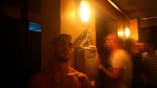 A gay bar in Israel with a shirtless man leaning against the wall