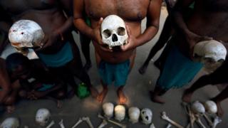A row of men hold skulls.
