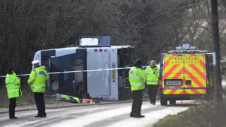 A bus overturned on the side of a road with police vehicles around it