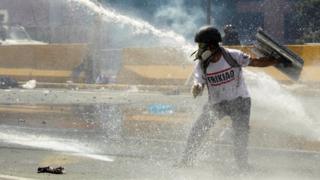 Manifestante recibe un chorro de agua de un carro hidrante.