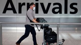 Man wearing a face mask walking through arrivals at Heathrow Airport