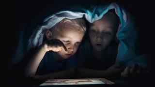 Маленькие дети, глядя на планшетный компьютер под одеялом