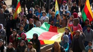 Kurdish people carry flags as they march during a protest in the city of al-Derbasiyah, on the Syrian-Turkish border, against what the protesters said were the operations launched in Turkey by government security forces against the Kurds