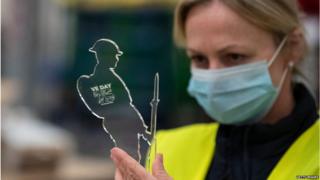 Worker in mask preparing a 'Tommy' figure as part of VE day commemorations at Royal British Legion factory