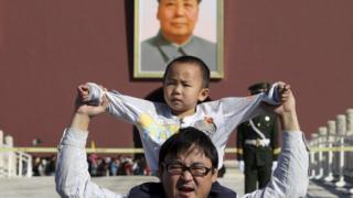 Мальчик сидит на плечах отца, фотографируя перед гигантским портретом покойного китайского председателя Мао Цзэдуна у ворот Тяньаньмэнь в Пекине, Китай, 2 октября 2011 года.