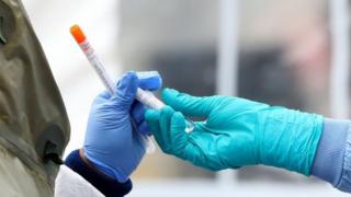 Medical professionals pass each other a coronavirus test at a drive-thru testing site at Cambridge Health Alliance Somerville Hospital on April 28, 2020 in Somerville, Massachusetts.