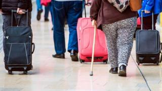 Pasajeros con sobrepeso que caminan en una aeropuerto, vistos de espaldas