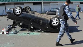Russian riot policeman passes by an overturned car after a mass brawl at the Khovanskoye cemetery in Moscow, Russia, 14 May 2016.