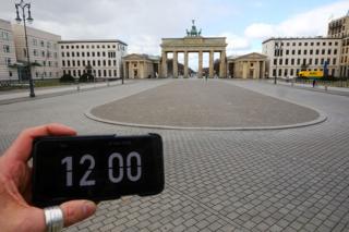 A digital clock on a smartphone is pictured in front of Brandenburg gate, Berlin, Germany.