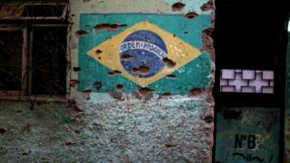 Parede com bandeira do Brasil marcada por balas; propostas de Jair Bolsonaro e Fernando Haddad para violência vão de liberação de posse de armas a investigação tocada pela Polícia Federal