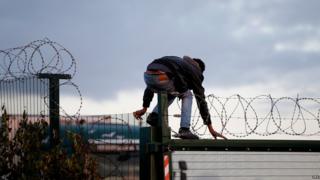 Migrants climbs over the fence to try to catch a train to reach England