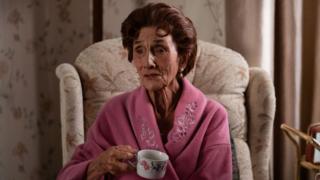 June Brown as Dot Branning in EastEnders, sitting in an armchair drinking a cup of tea