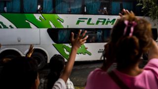 Crianças acenam para pessoas dentro de um ônibus saindo