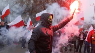 A masked participant holds up a flare prior to the planned March of Independence to mark the 100th anniversary of the reinstatement of Polish independence in Warsaw, 11 November 2018