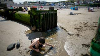 A child plays near a storm overflow pipe on Borth Beach, Wales