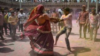 Indian Hindu's covered in coloured powder dance as they celebrate Holi,