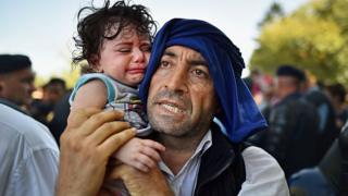 A man holds his crying child close to him as migrants force their way through police lines at Tovarnik station for a train to take them to Zagreb on September 17, 2015 in Tovarnik, Croatia.