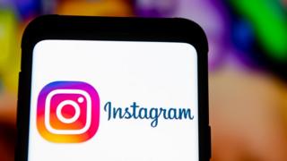 El logotipo de Instagram se ve en la pantalla de un teléfono móvil frente a una pantalla vívida pero borrosa.