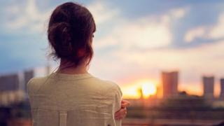 Una mujer de espaldas a la puesta de sol.