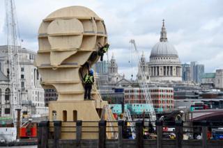 Workmen install a sculpture called Head Above Water in London