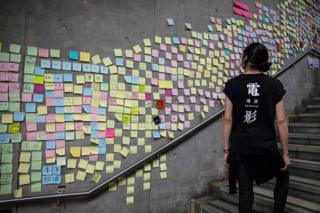 A woman walks past a wall in Hong Kong covered with sticky note messages