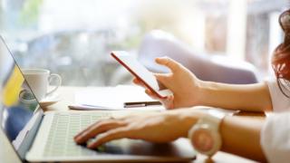 Young woman looking at smartphone while using laptop