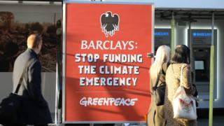 People walk past a Greenpeace protest at a Barclays branch