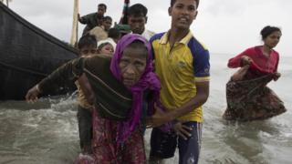 Молодой мужчина рохинджа несет пожилую женщину, после того, как деревянная лодка, на которой они ехали из Мьянмы, врезалась в берег и опрокинула всех в Дахинпара, Бангладеш