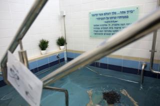 A Jewish woman enters the water of a mikva in Jerusalem on April 17,2019. (Photo by Heidi Levine for The BBC).