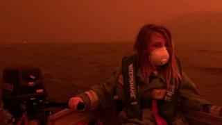 A primary-school aged Australian boy wears a mask and life vest in a in a boat on Mallacoota lake after his family fled into the water to escape the bushfire threatening the town on 31 December 2019