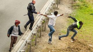 Un policier asperge du gaz lacrymogène à des migrants qui tentent d'accéder au tunnel sous la Manche, en juin 2015, dans le nord de la France.
