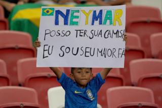A boy holds up a handmade sign in the stands at a football match.
