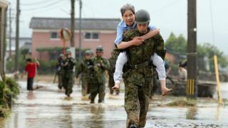 young soldier carrying older civilian in piggyback over wet ground